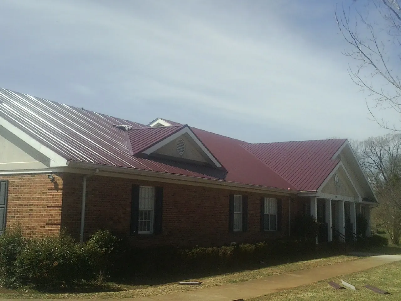 Red metal roof with gabled entries on a long brick building, from a Hail Damage Roof Repair job in Tiplersville