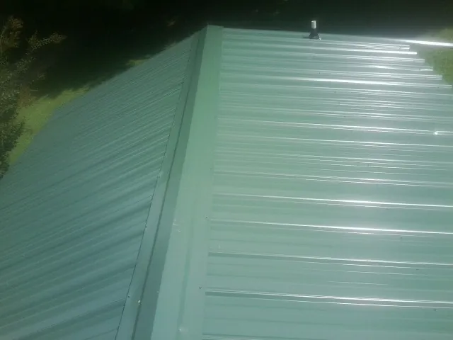 New green metal panels meeting at the ridge of a roof — Flat Roof Repair work by our crew in Tiplersville
