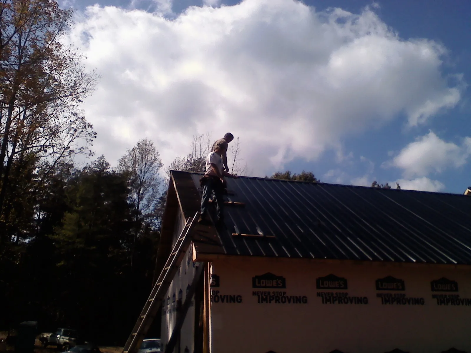 Roofer fastening dark metal panels high against a cloudy sky, from a Roof Inspection job in Tiplersville