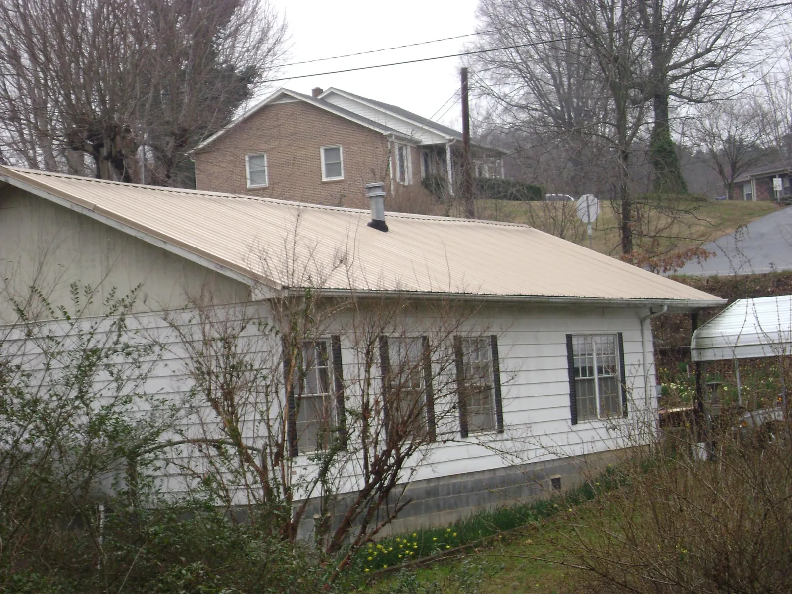 Tan metal roof on a white sided house set into a hillside — Commercial Roofing by Roofing Brothers in Tiplersville